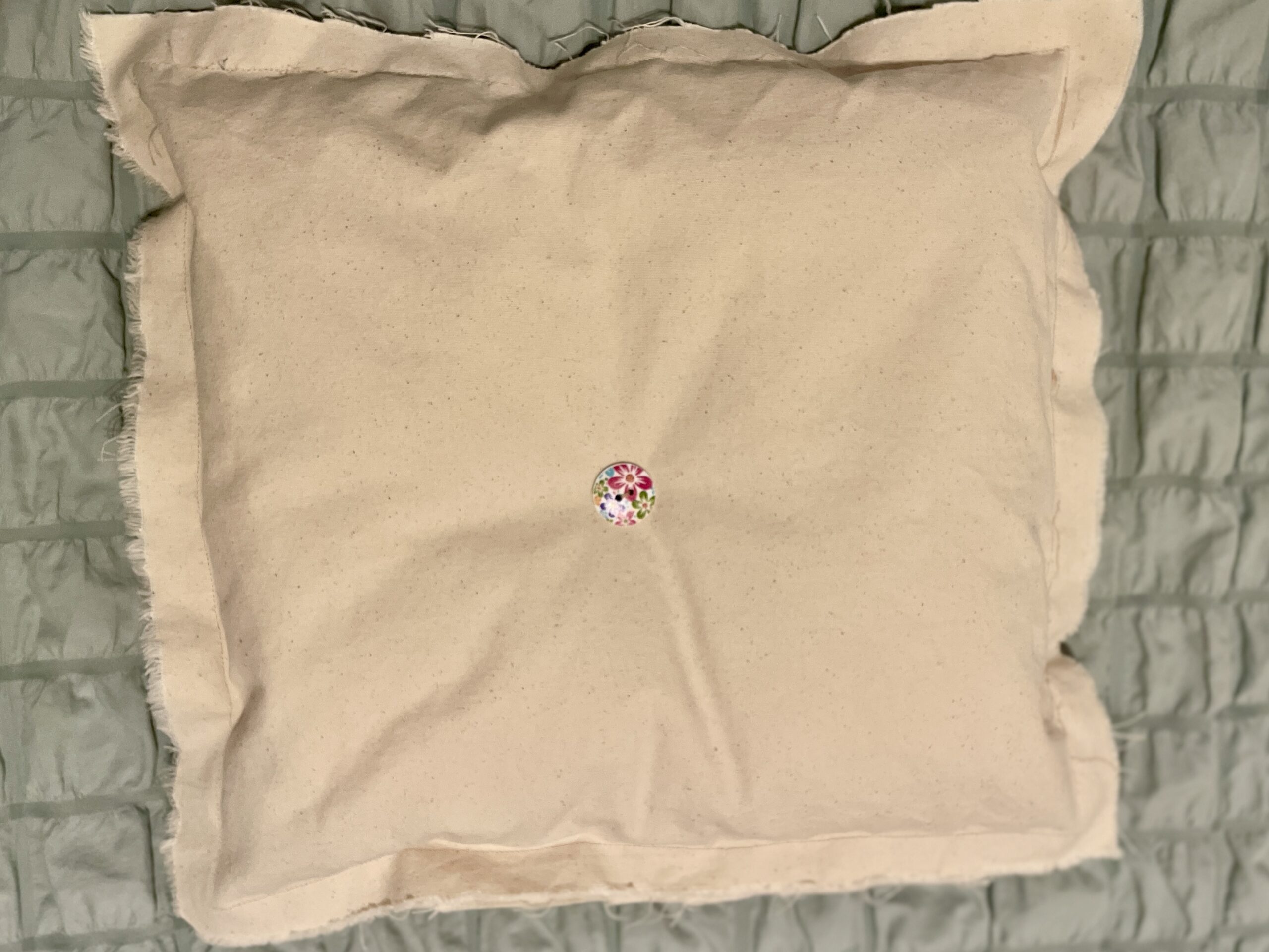 Beige pillow with frayed edges and floral button