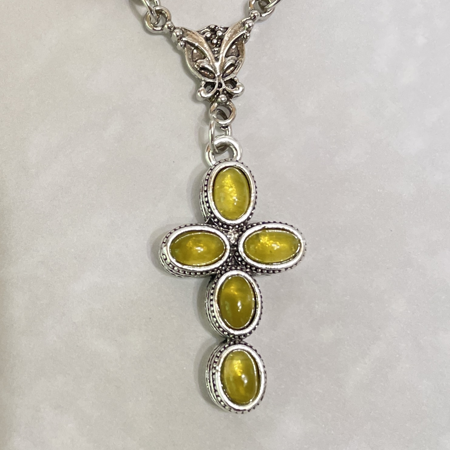 Silver cross pendant featuring yellow oval stones