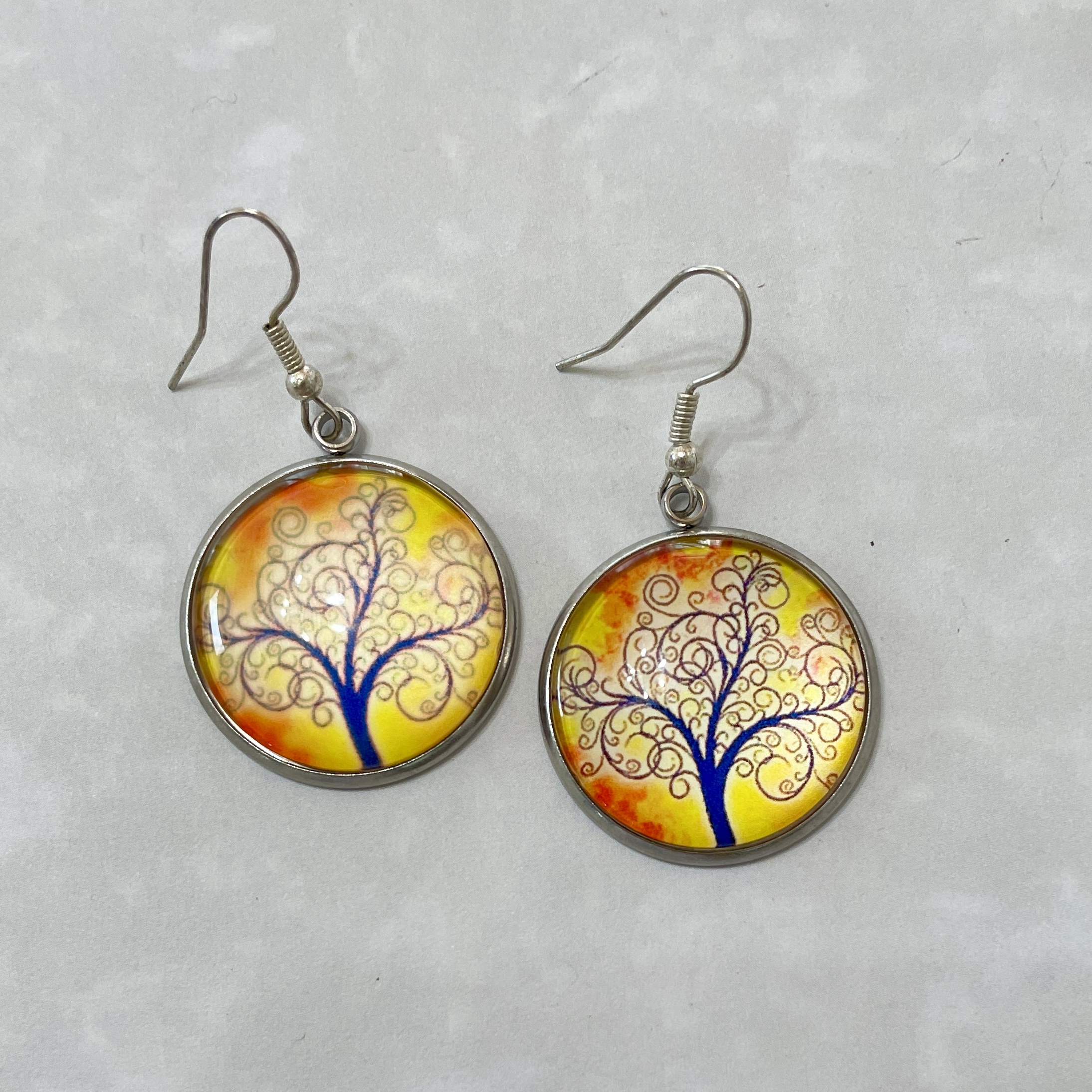 Round earrings with blue tree on yellow background