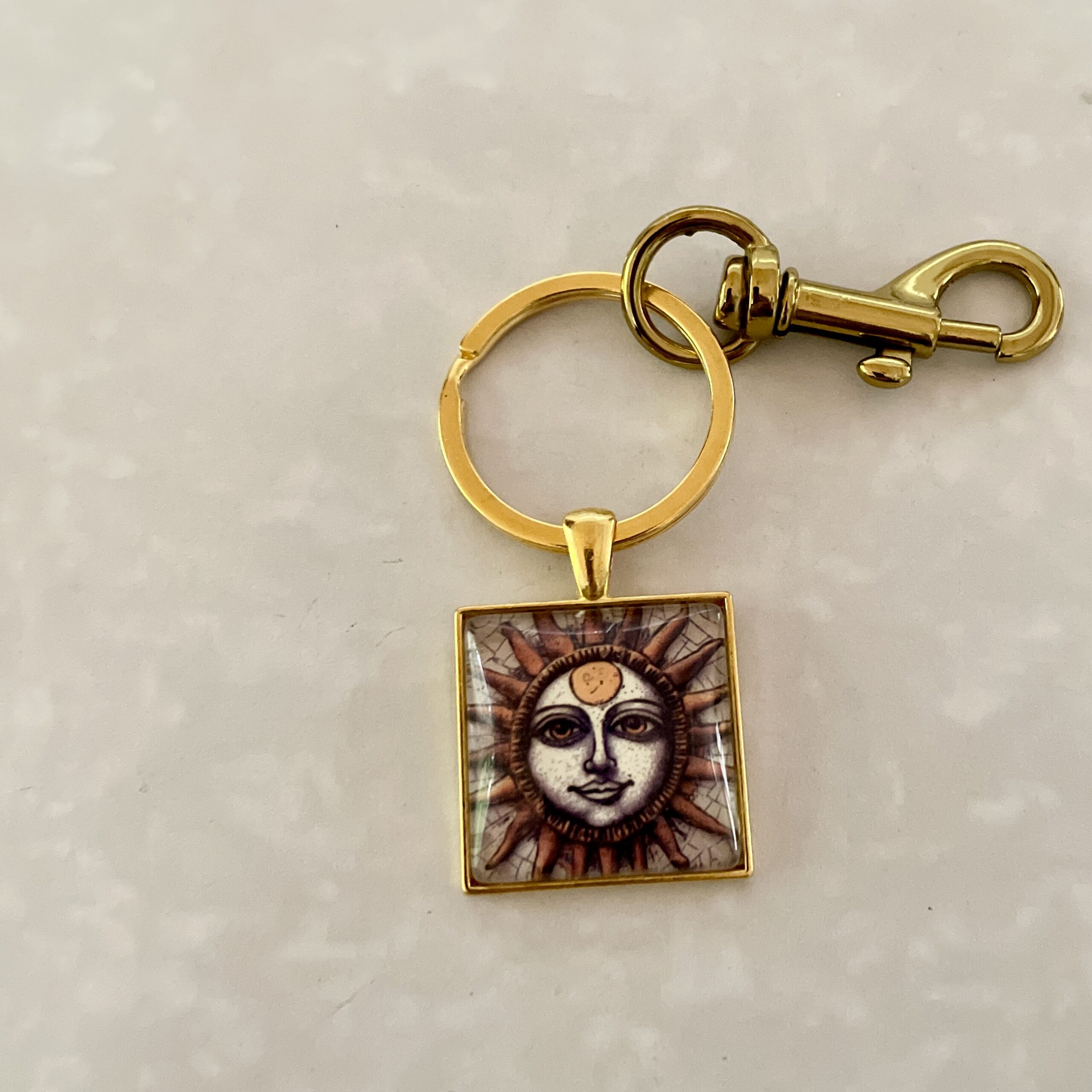 Gold keychain with sun motif pendant.